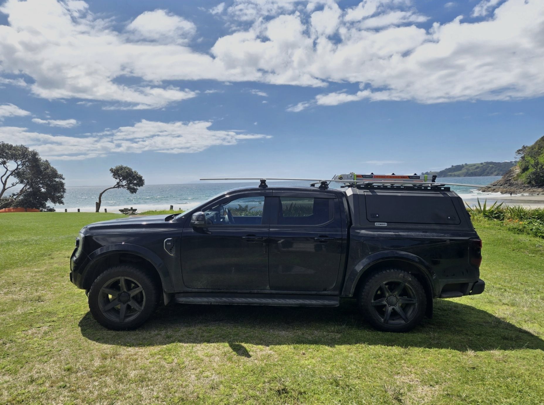 The black Rodney Electrical ute parked on the grass beside a Rodney beach